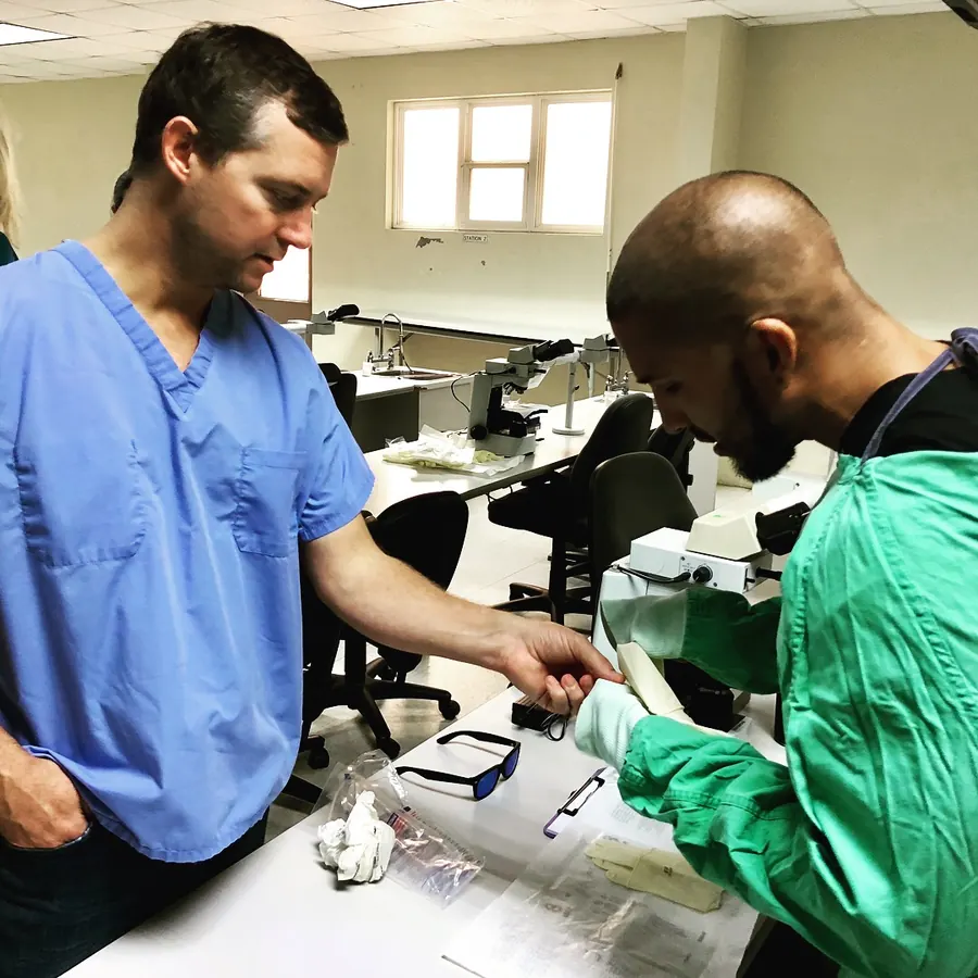 El Dr. David Arias con bata verde trabajando en un laboratorio junto a un instructor durante su formación veterinaria