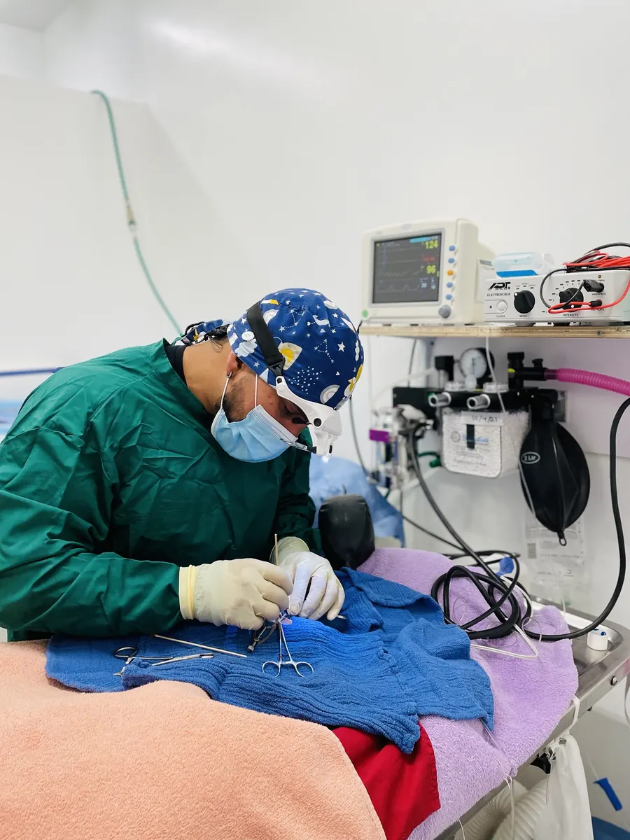 El Dr. David Arias con gorro y bata quirúrgica realizando un procedimiento, con equipo de monitoreo de anestesia a su lado