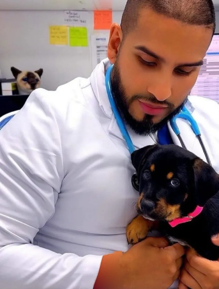 Dr. David Arias, DVM, in a white coat with a stethoscope, gently holding a black and tan puppy